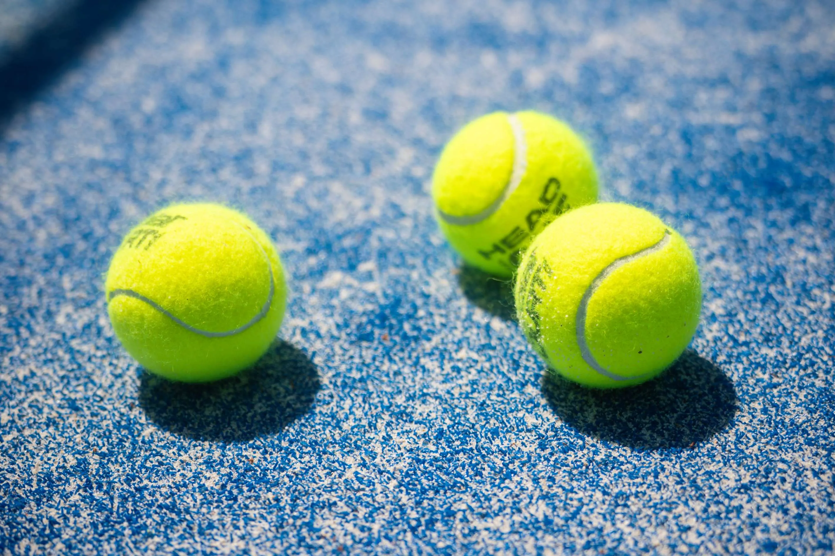 Drei Padel-Bälle auf einem blauen Court-Belag