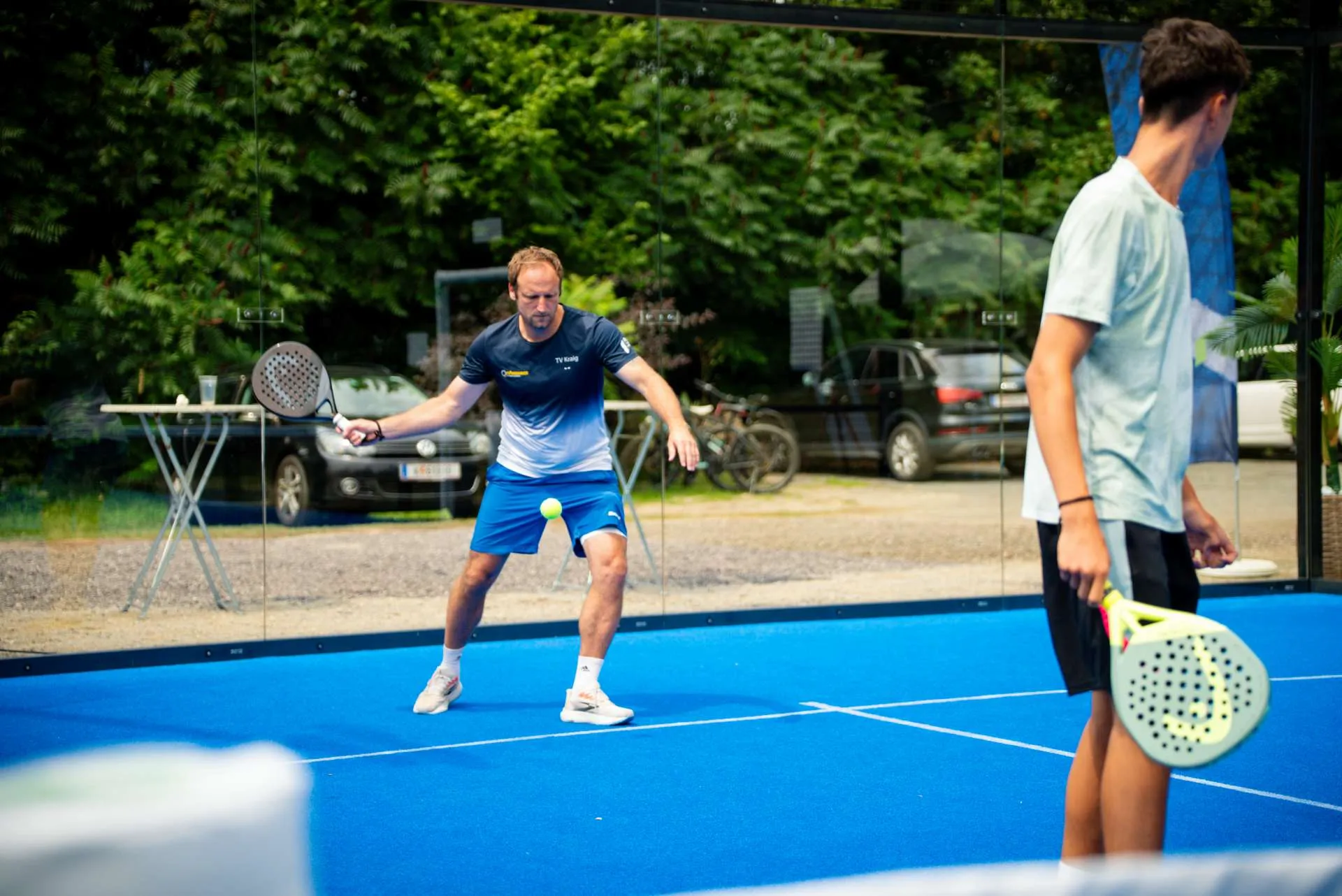 Zwei Spieler im Ballwechsel vor der Glaswand eines Padel-Courts
