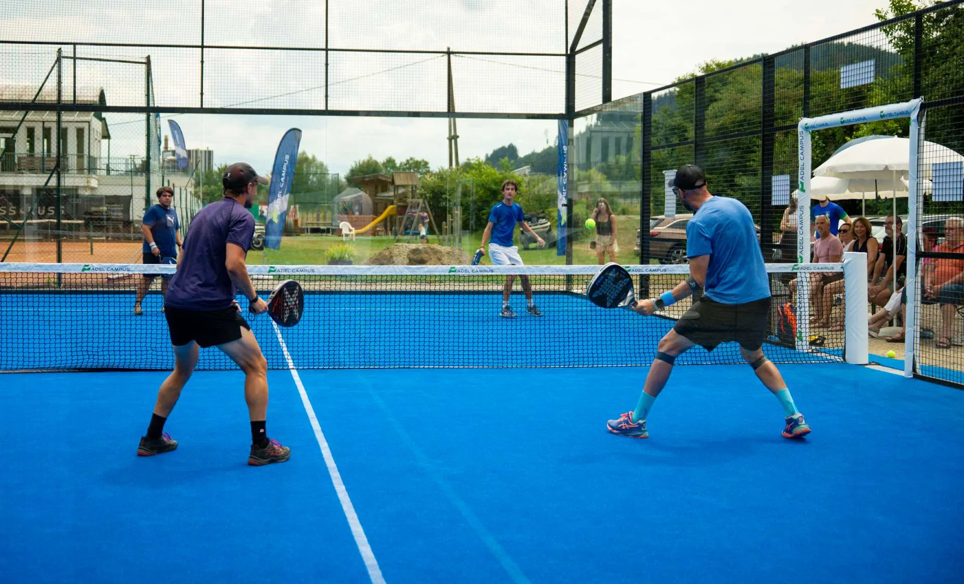 Vier Spieler beim Padel-Doppel auf einem blauen Outdoor-Court